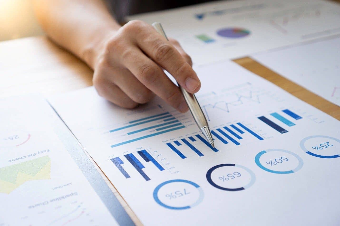 Hand holding a pen pointing to a bar chart on a paper that has multiple charts. 