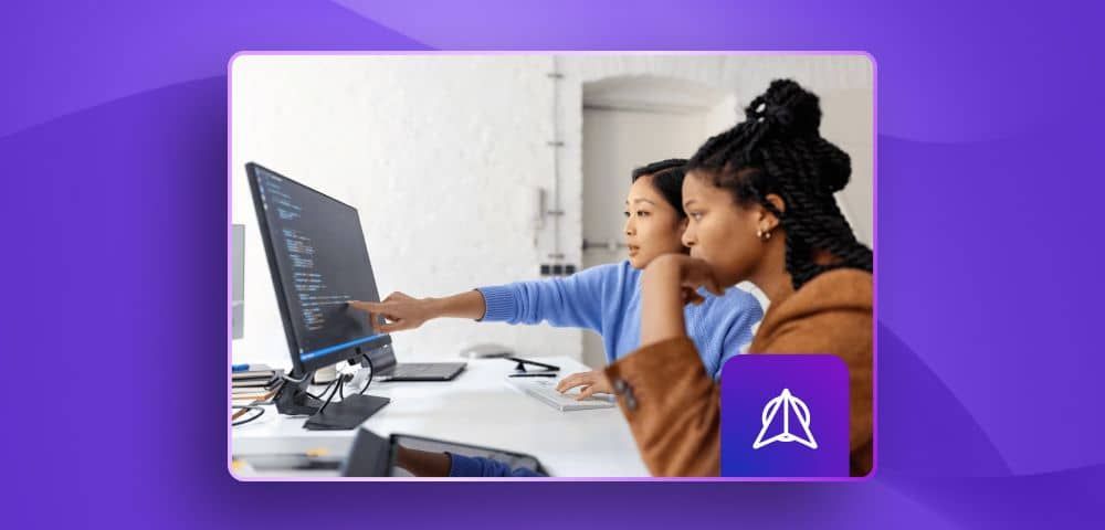 two women looking at a screen with code in it, in an office desk