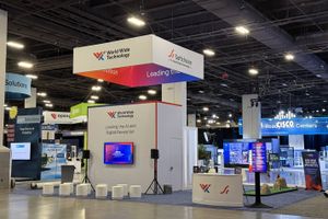 A World Wide Technology and Softchoice convention booth inside a large expo hall. The booth features a white structure with a digital screen displaying "Leading the AI and Digital Revolution," surrounded by small white cylinder seats, a reception desk, and a hanging overhead sign
