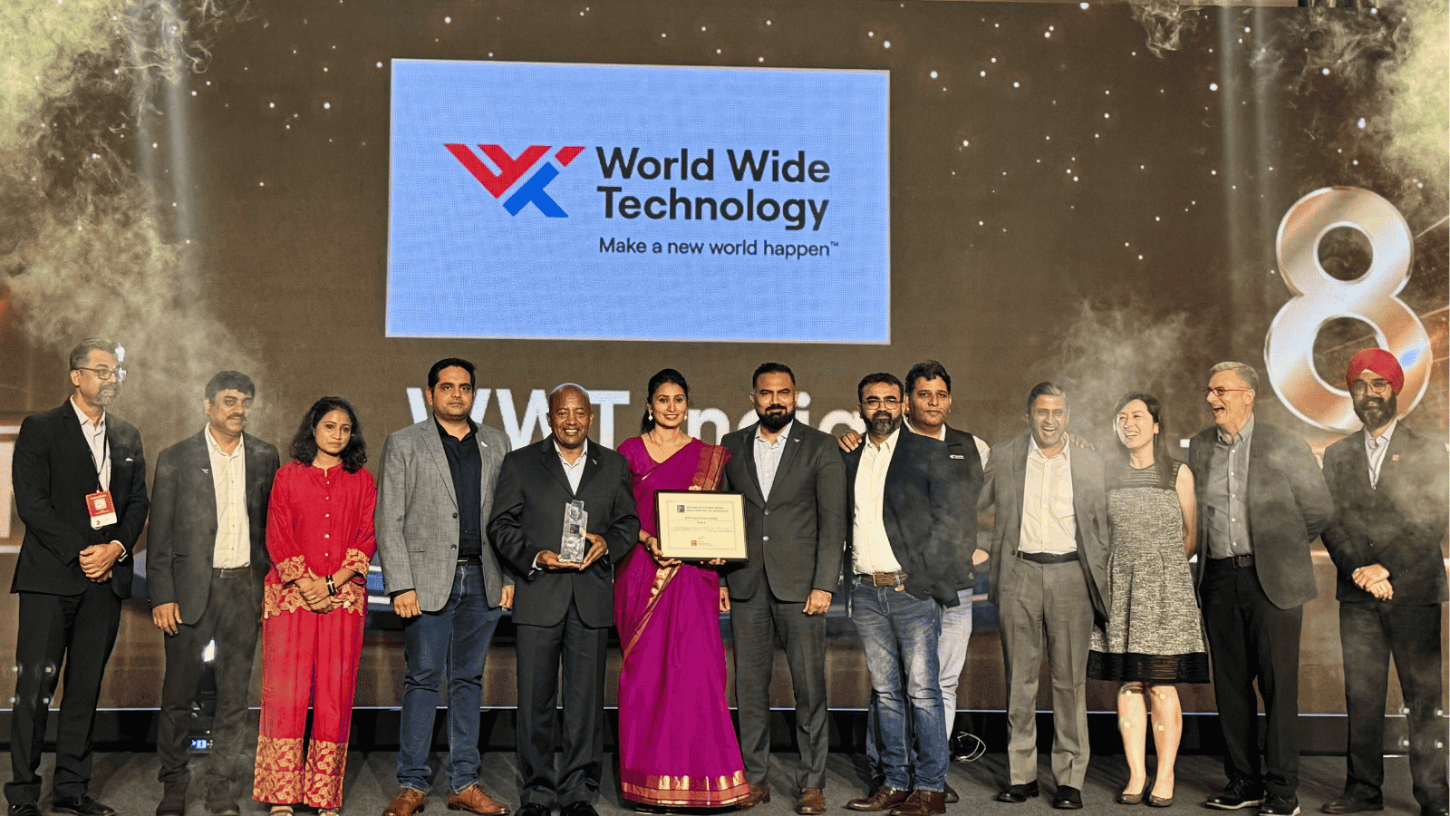 A group of people smile and gather together on a stage with an award. The World Wide Technology logo and the number 8 is visible in the background.