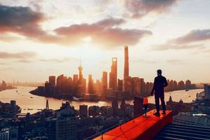 Man standing on red bridge looking over sunset on large city skyscrapers