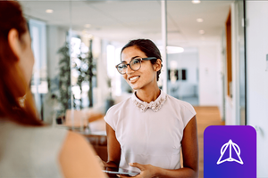 A picture of a smiling woman who is wearing glasses and holding a tablet in an upscale, warm office environment. The WWT Research logo is overlaid on the image.
