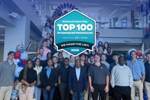Group photo of dozens of interns gathered on a staircase and in a lobby, with red, white and blue balloon displays and an overlaid badge recognizing a 2026 Top 100 Internship Program by Yello and WayUp.