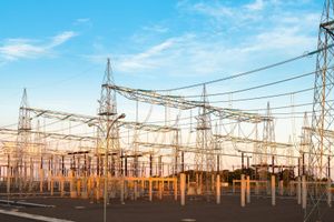 Electrical power substation with transmission towers, transformers and high-voltage lines supporting the electric grid under a clear blue sky.