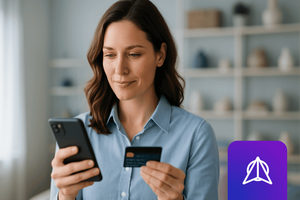 A woman looking at her smartphone while holding a credit card, shopping online in a bright home setting.