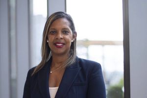 Professional headshot of a person wearing a navy blazer, standing in front of a window.