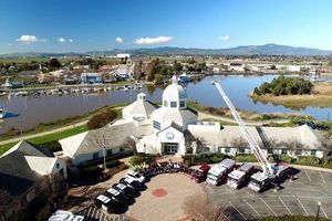 Aerial view of Suisun City Hall beside a waterfront marina, with emergency vehicles and a raised fire truck ladder gathered outside.