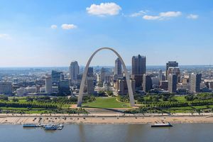 St. Louis skyline viewed from across the Mississippi River, featuring the Gateway Arch centered in front of downtown buildings under a clear blue sky.