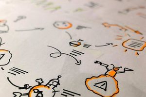 Close-up photo of hand-drawn marker doodles on paper, including robots, speech bubbles and arrows, in black and orange ink.