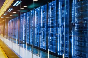 Server racks with blue LED lighting line a glass-enclosed data center aisle, highlighting rows of networking and computing infrastructure.
