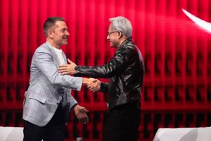 Two people shake hands on a stage with a vivid red backdrop, highlighting a partnership or collaboration during a public event.