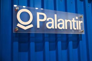 Palantir logo displayed on a clear acrylic sign mounted to a blue corrugated wall.