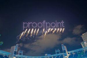 Night view of a stadium from below, with fireworks bursting beneath a drone light show that spells out the Proofpoint logo in the sky.