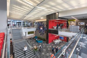 Wide shot of WWT's global headquarters with employees walking throughout the lower level floor and up the stairs to the main level. Shows glass wall conference rooms with people meeting inside them.