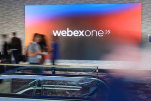 Blurred attendees pass in front of a colorful WebexOne 26 conference display near an escalator.